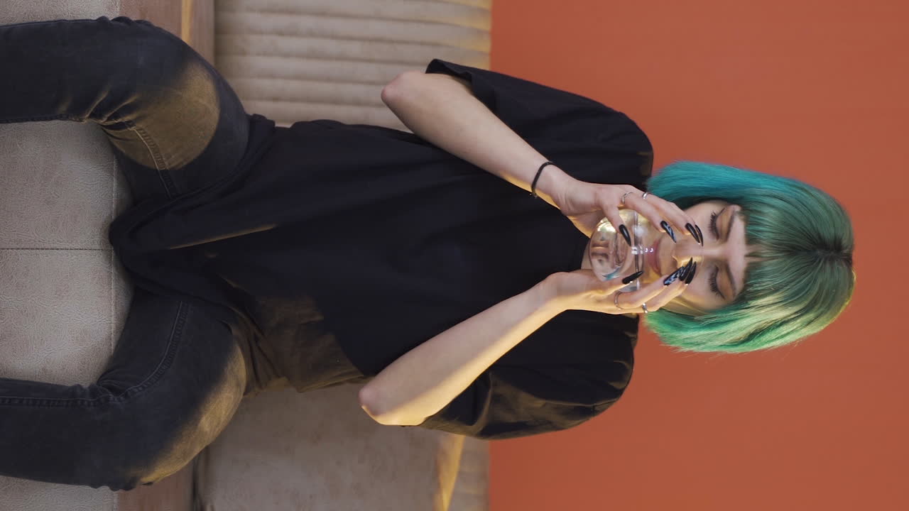 vídeo vertical de una joven cobarde bebiendo agua con la mano temblorosa.