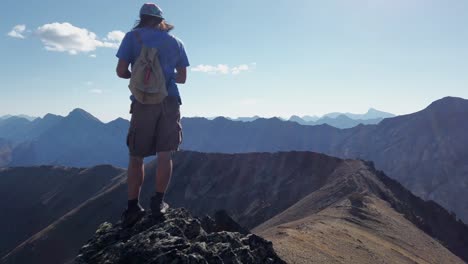 Hiker-on-peak-taking-photos-mountain-range-pan-Kananaskis-Alberta-Canada