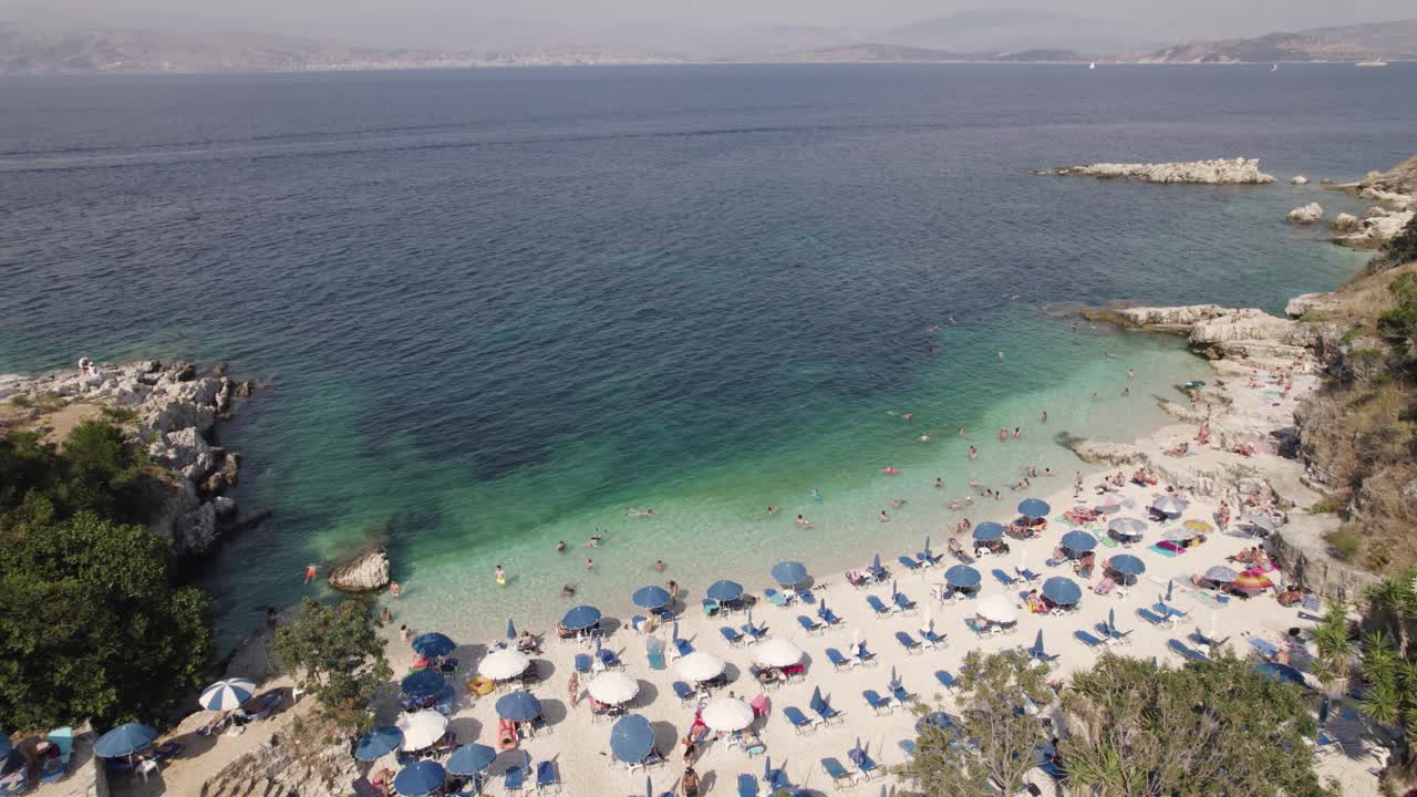 Beautiful greek pebble beach with blue umbrellas and turquoise water, Corfu Island