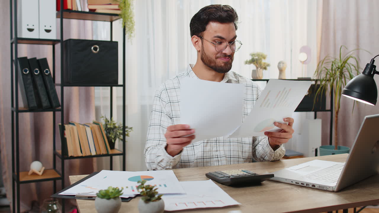 Focused indian office worker working with schedules and financial graphics while using calculator