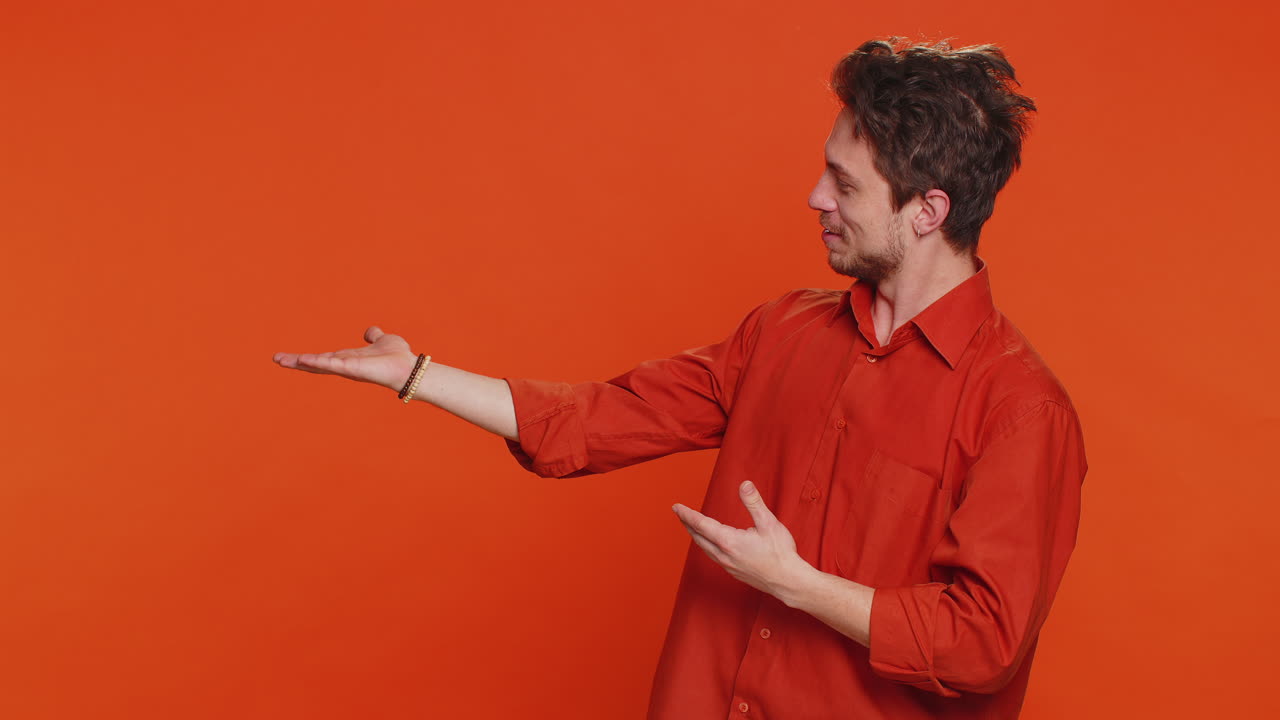 joven mostrando los pulgares hacia arriba y señalando a la izquierda en el espacio en blanco lugar para su logotipo de publicidad