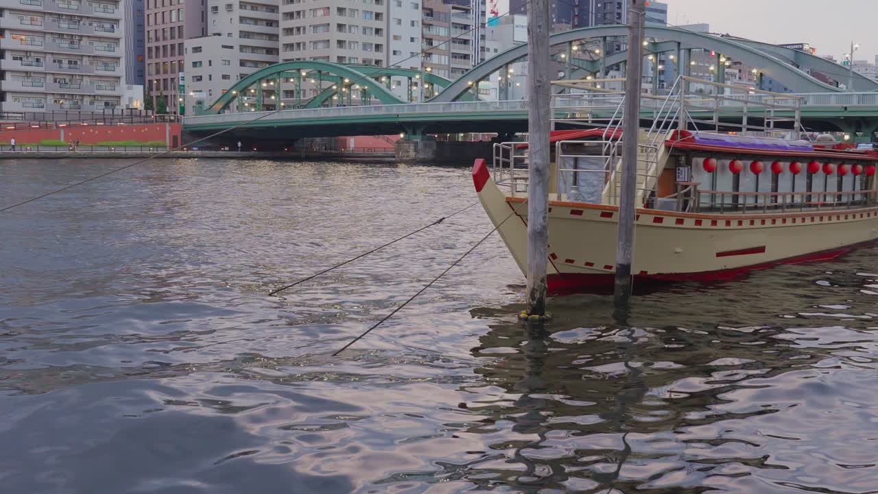 Houseboats float on the Sumida River with the lit-up Komagata Bridge in the background at dusk