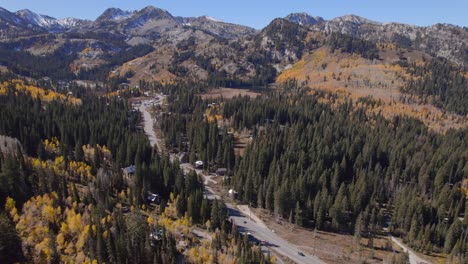pan de barrido de un camino que entra en las montañas cubiertas de nieve y rodeado de álamos amarillos con otros colores de otoño