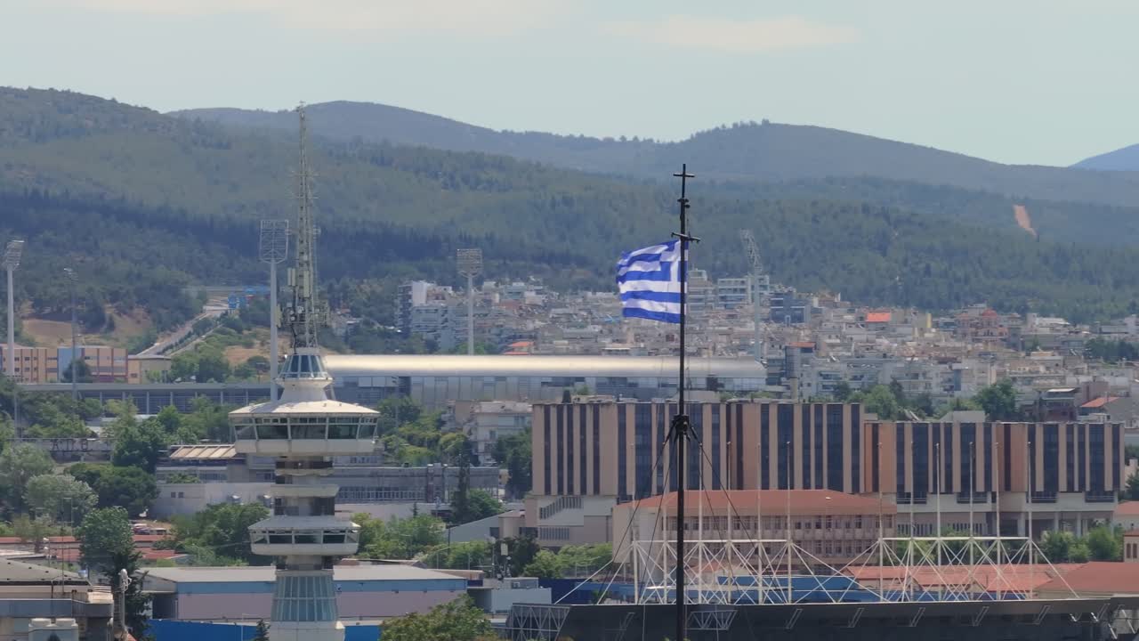 Greek flag waving with telecommunications tower and mountains of Thessaloniki in the background