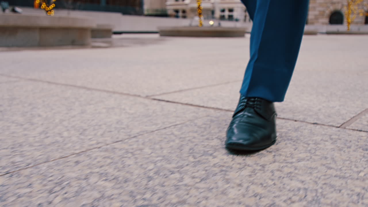 Close up of businessman shoes walking on plaza. Close-up of black dress shoes and blue suit trousers walking on stone pavement in New York plaza