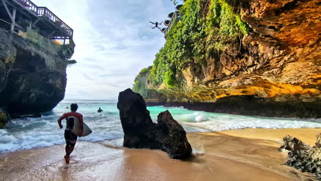 surfers runs into ocean water in uluwatu beach, drone flying above, slow motion