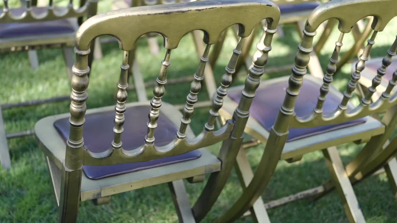 Élégantes chaises de mariage dorées disposées en rangées sur l’herbe, prêtes pour une cérémonie en extérieur.