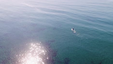 drone flying on the mediterranean sea, birds eye view over a paddleboarder rotating into the horizon