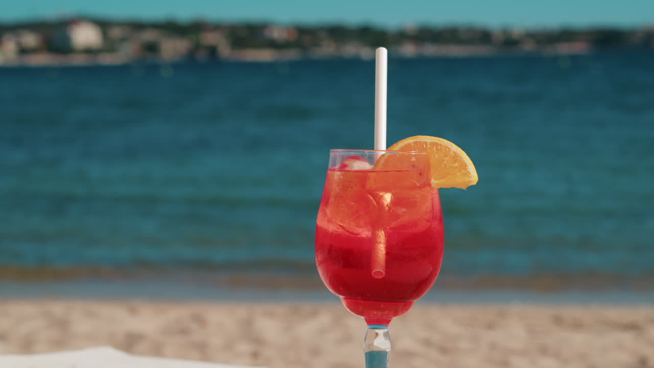 Un cocktail rinfrescante rosso-arancio con ghiaccio e fetta d'arancia sullo sfondo del blu intenso del Mar Mediterraneo