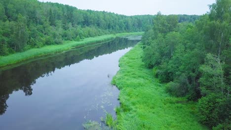 aerial view of a venta river on a sunny summer day, lush green trees and meadows, beautiful rural landscape, wide angle drone shot moving backward