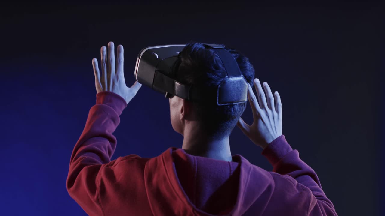 Asian man using vr headset, touching virtual screen on blue background, slow motion