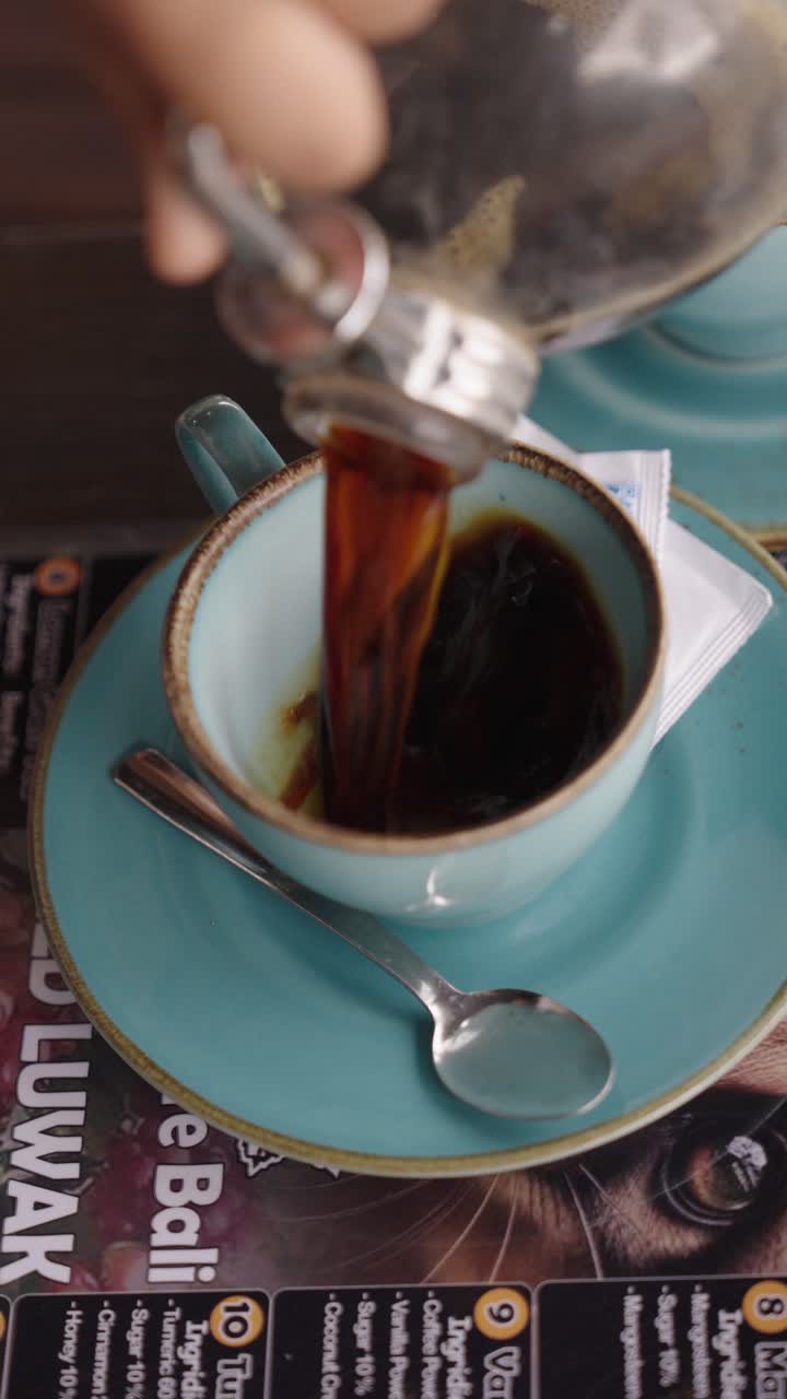 Pouring freshly brewed coffee into cup, close-up vertical view