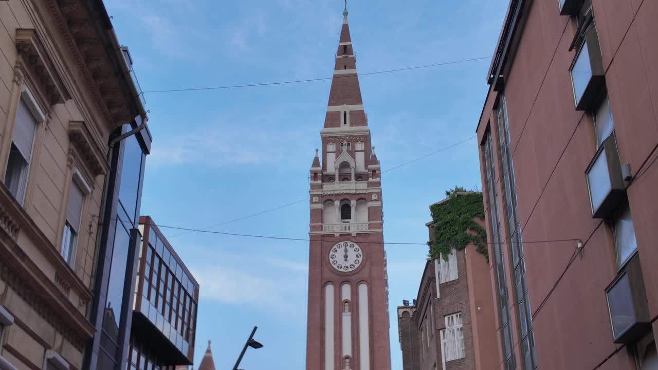 Distant street view of Szeged’s Votive Church framed by buildings on either side, showing its towering presence in the cityscape