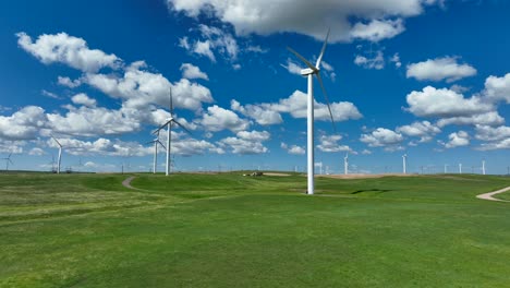 Low-aerial-glide-over-green-grass-with-tall-windmills-spinning-on-windy-day