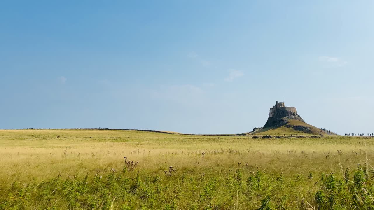 Blue sky over agricultural fields with a distant view towards Lindisfarne Castle on Holy Island, showing rural landscape and historic North East coast on a clear day