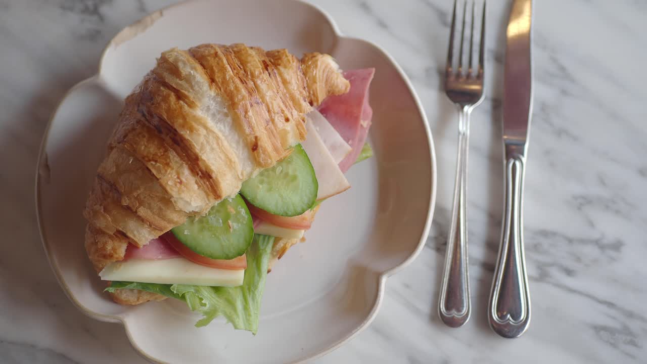 Primo piano di un delizioso croissant salato con prosciutto, formaggio, lattuga, pomodoro e cetriolo