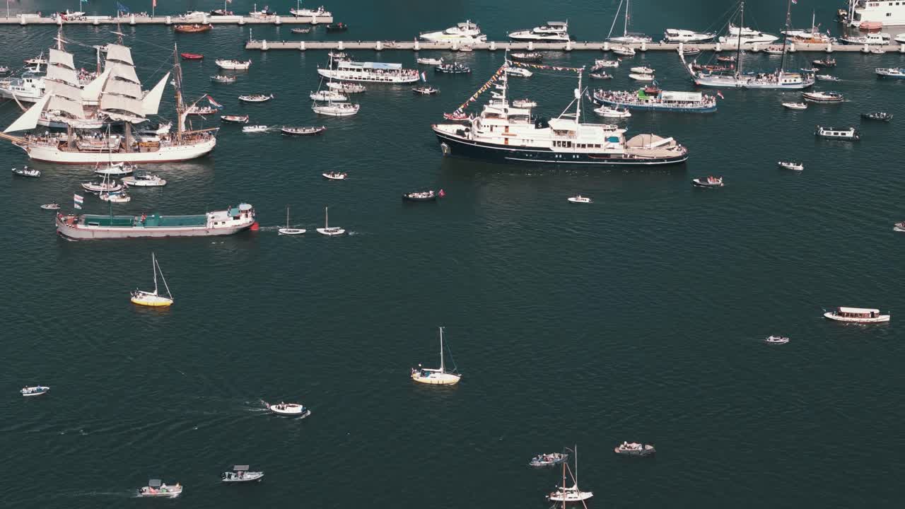 Aerial shot tracking right as small boats pass tall ships moving the opposite way