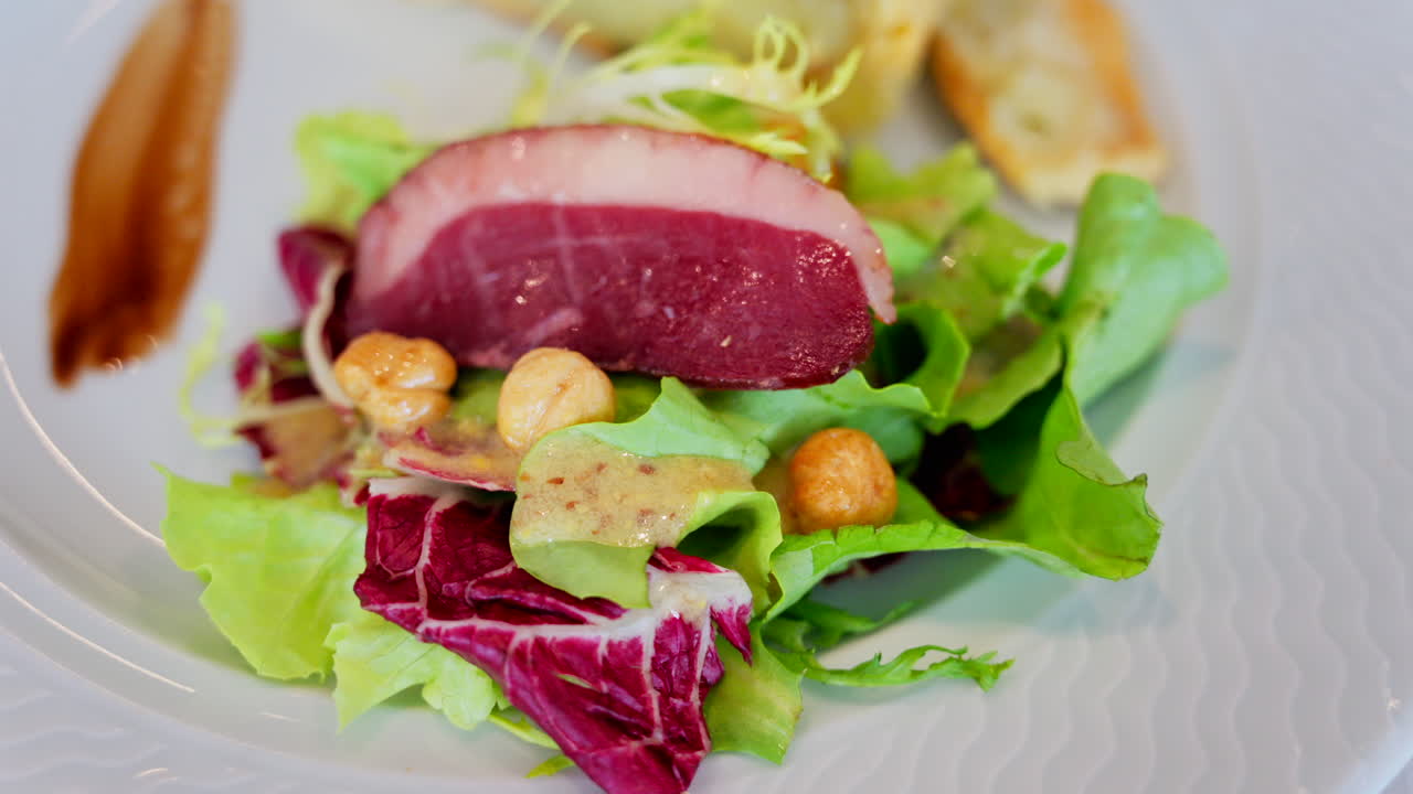 Close up of a slice of quiche featuring with a side salad and a slice of cured meat on a white plate at a restaurant