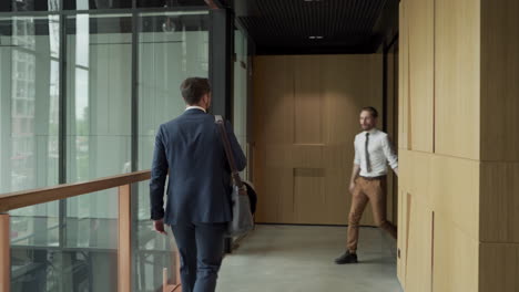 un attraente giovane uomo d'affari cammina attraverso un corridoio con una borsa da uomo. incontra un collega che porta un carrello. lo saluta e iniziano a parlare. i goth sono in viaggio di lavoro