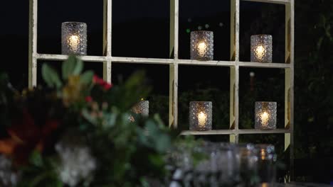 un estante metálico de oro con velas encendidas en recipientes de vidrio que decoran una recepción de boda por la noche