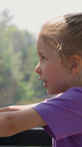 amazed little female child in purple t-shirt looks at mountains and talks in cabin with large window of cable way close side view slow motion