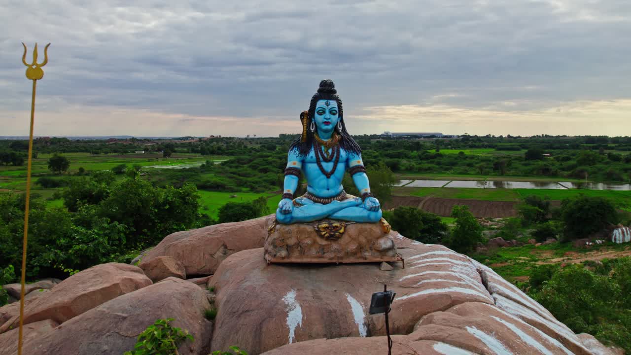 hindu god shiva statue with granite stone and farming land, push in shot, drone shot, 4k.