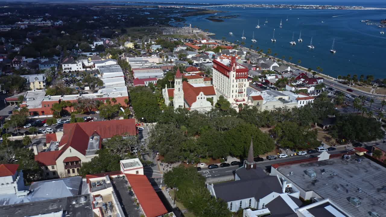 Historiskt område vid vattnet med distinkt arkitektur med röda tak har utsikt över lugnt vatten med förankrade segelbåtar och omgivande urban grönska under en klar himmel
