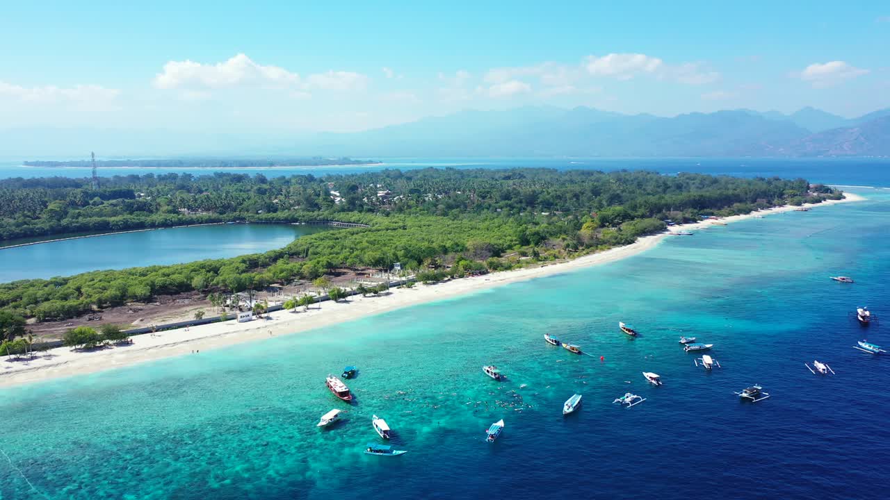 Tropical island with wide white exotic beach washed by calm turquoise lagoon where many boats floating near shore of tropical island with resorts in Bali