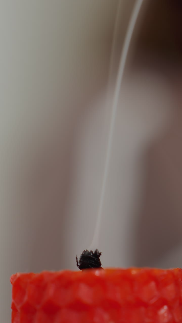 primer plano extremo de la llama de la vela roja que se apaga, con una figura borrosa en el fondo, las brisas de humo se elevan a medida que la llama se desvanece, creando una atmósfera calmante y reflexiva