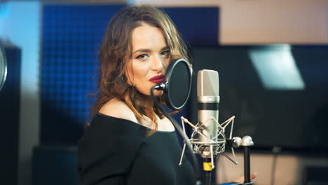 beautiful playful singer at the professional microphone in audio studio. attractive woman singing happily into the mic indoors. female voice.