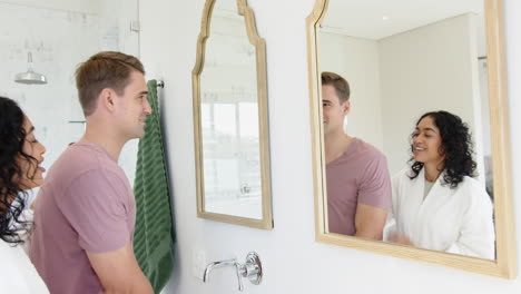 young multiracial couple in bathroom, man washing hands while asian woman looks in mirror, at home