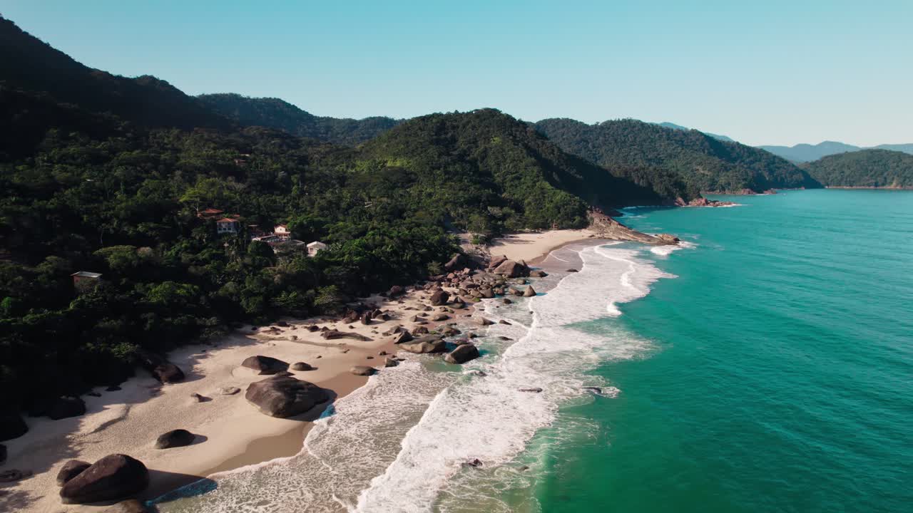 Stunning aerial view of a secluded, rocky Brazilian beach with pristine sand and clear turquoise water. Backed by dense Atlantic Forest mountains, it's perfect for themes of luxury travel, escape