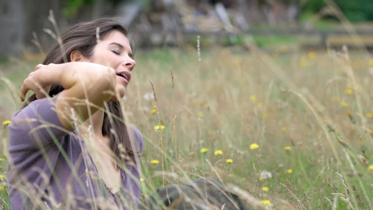 Lovely young woman plays with her brunette hair while relaxing in a beautiful field of sunny flowers