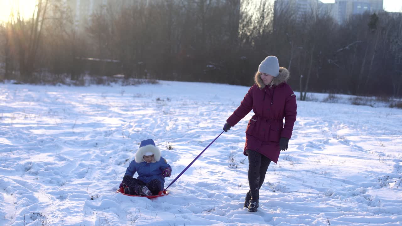 concepto de familia, trineo, temporada y personas - madre feliz tirando de trineo de hielo con el niño al aire libre en invierno