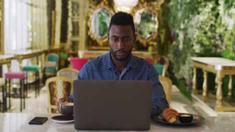African-american-businessman-using-laptop-drinking-coffee-in-cafe