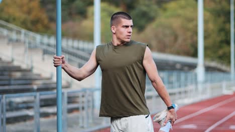 sporty young man stretching on bar on rattling track of sports facility