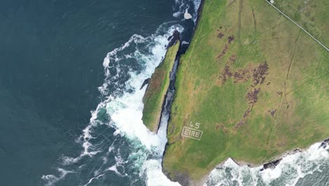 rugged irish coastline with waves crashing, marked with 'éire' signat loop head, rolling aerial shot