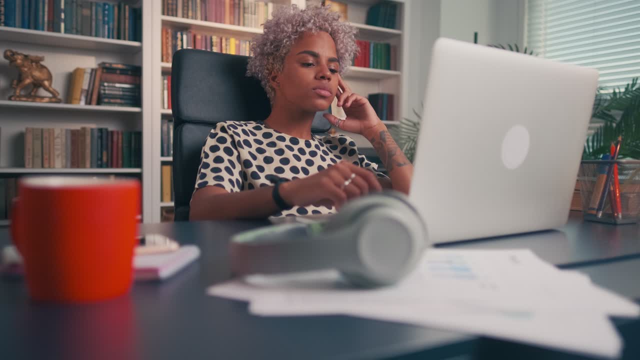 Serious focused young woman working on laptop while sitting in home office