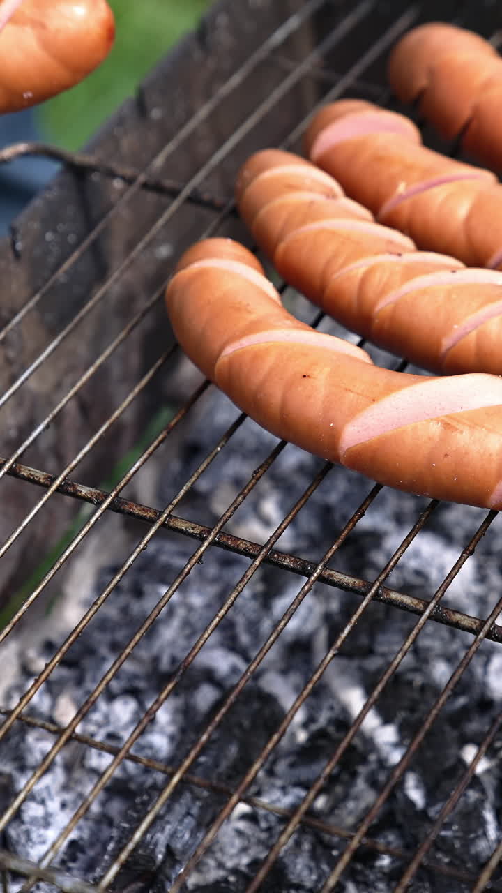 Preparation for grilling sausages. Sausages with incisions on the grill. Process of preparing tasty hot dogs. Barbeque outdoors. Time for picnic. Vertical video