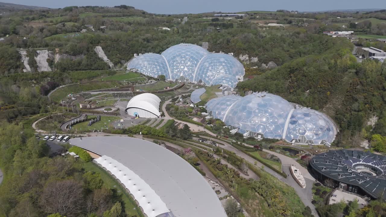 Panoramic aerial of interconnected Eden Project biomes sparkling above concentric botanical terraces and forested quarry walls, celebrating ecological education and climate innovation
