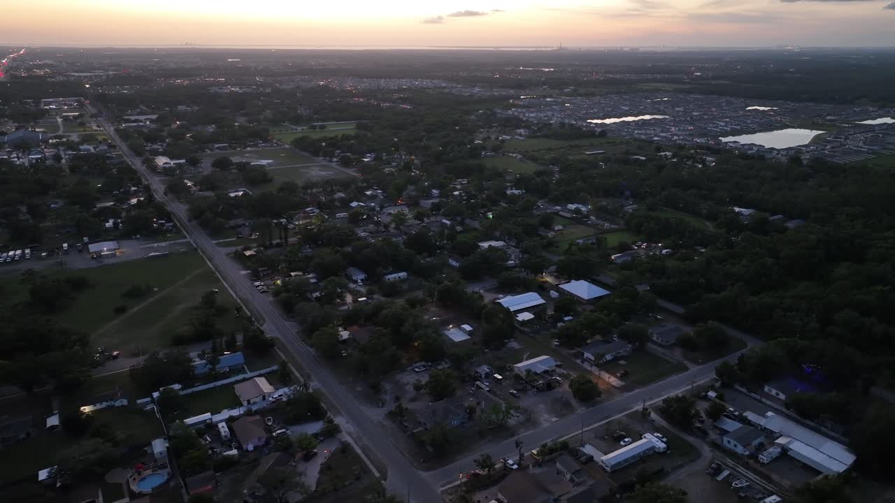 High angle drone shot over American town with luxury apartment district in distance. Private lake in center of neighborhood. Sunset time in sun city, Florida. Main Street leading to town