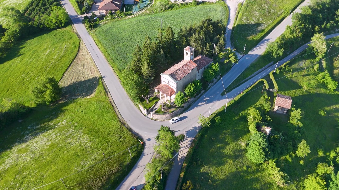 Korkealta kuvattu dronelaukkaus pienestä kirkosta ja autosta ajamassa läpi vihreän italialaisen maaseudun