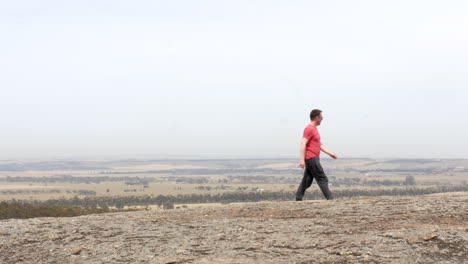 Man-walking-along-a-large-rock-high-up-on-a-mountain-in-Australia