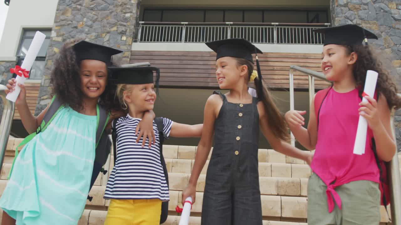 Video of happy diverse girls wearing graduation hats and holding diplomas