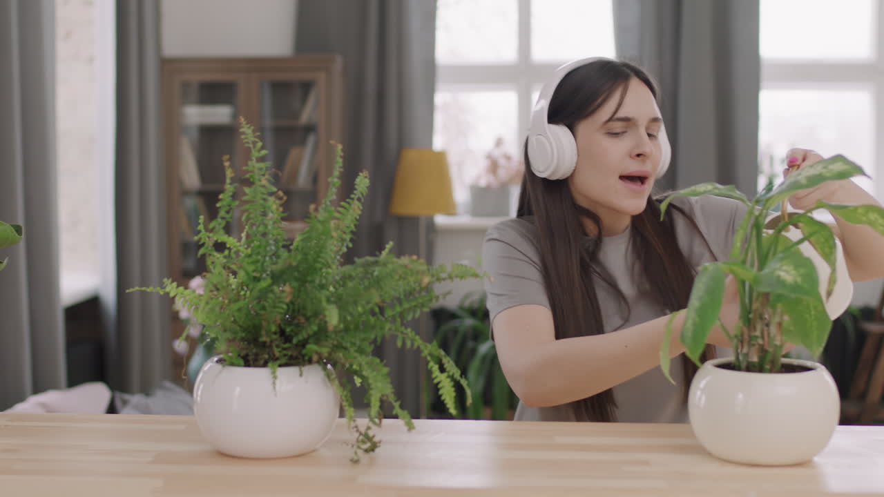 Woman in Headphones Listening to Music and Water Plants