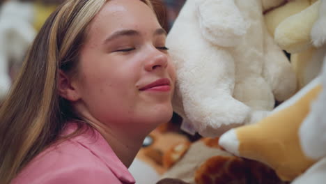 lady in pink dress rests her head on a soft white plush toy in a toy store, smiling and enjoying the cozy texture, surrounding her are other stuffed toys, neatly arranged on the shelve