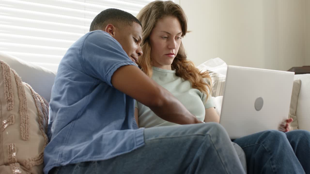 Homem digitando no teclado do laptop faz com que um casal diverso trabalhe rolando e apontando para a tela no sofá.
