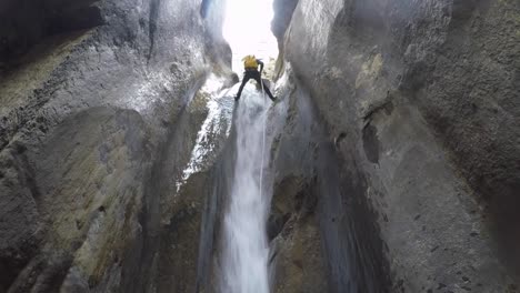 vista de ángulo bajo: hombre con paquete amarillo rappel cascada del cañón del río