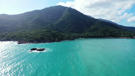 Turquoise-sea-water-washing-rocky-coastline-of-tropical-island-with-green-vegetation-hills-and-limestone-cliffs-near-shore-in-Myanmar