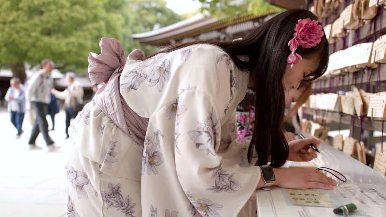Một người phụ nữ mặc kimono truyền thống viết lời ước nguyện lên một tấm bảng gỗ tại một ngôi đền.